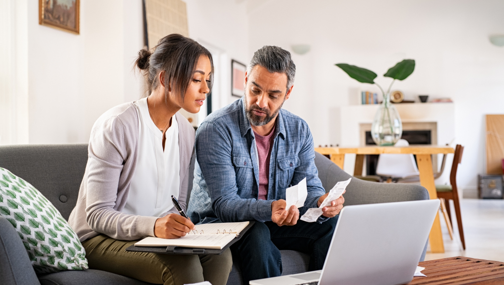 Couple sitting on a couch reviewing bills and receipts.