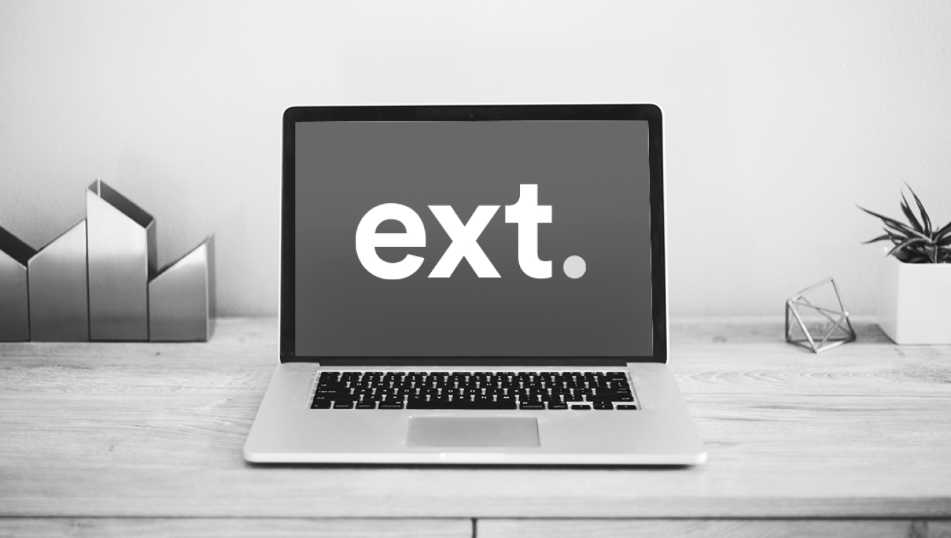 Laptop displaying the Ext. logo on a desk in black and white.