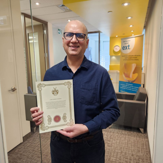 Ext. employee holding a framed certificate while standing in an office with a yellow banner in the background.