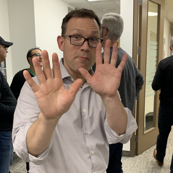 Ext. employee playfully holding up both hands with a humorous expression during a team event.