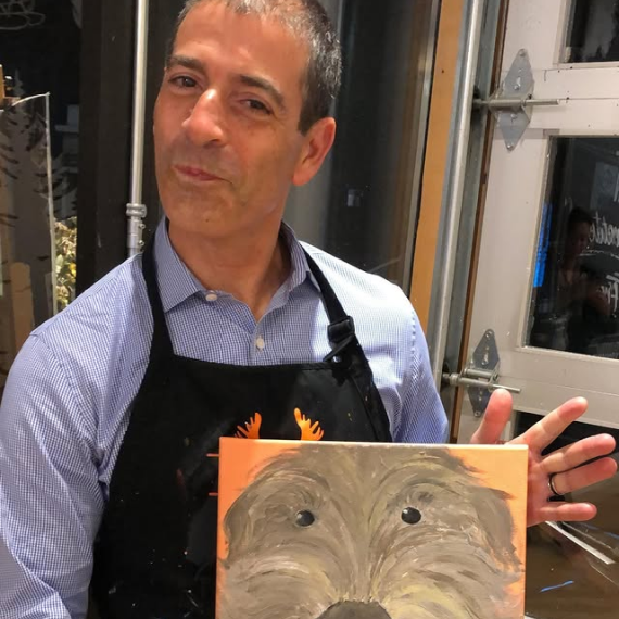 Ira Berg proudly displaying a painted canvas of a dog at a creative workshop event.