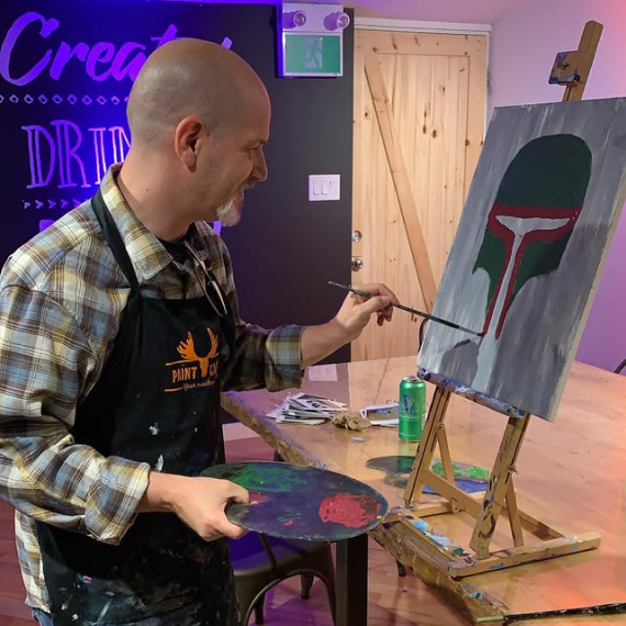 Richard Heft painting a detailed artwork of a Mandalorian helmet at a creative painting event.