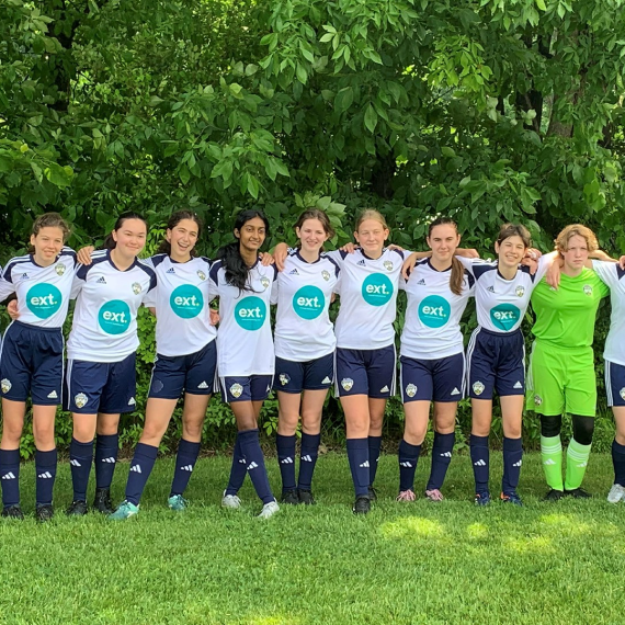 A soccer team posing together in their white jerseys with 'ext' logo, standing on a grassy field.