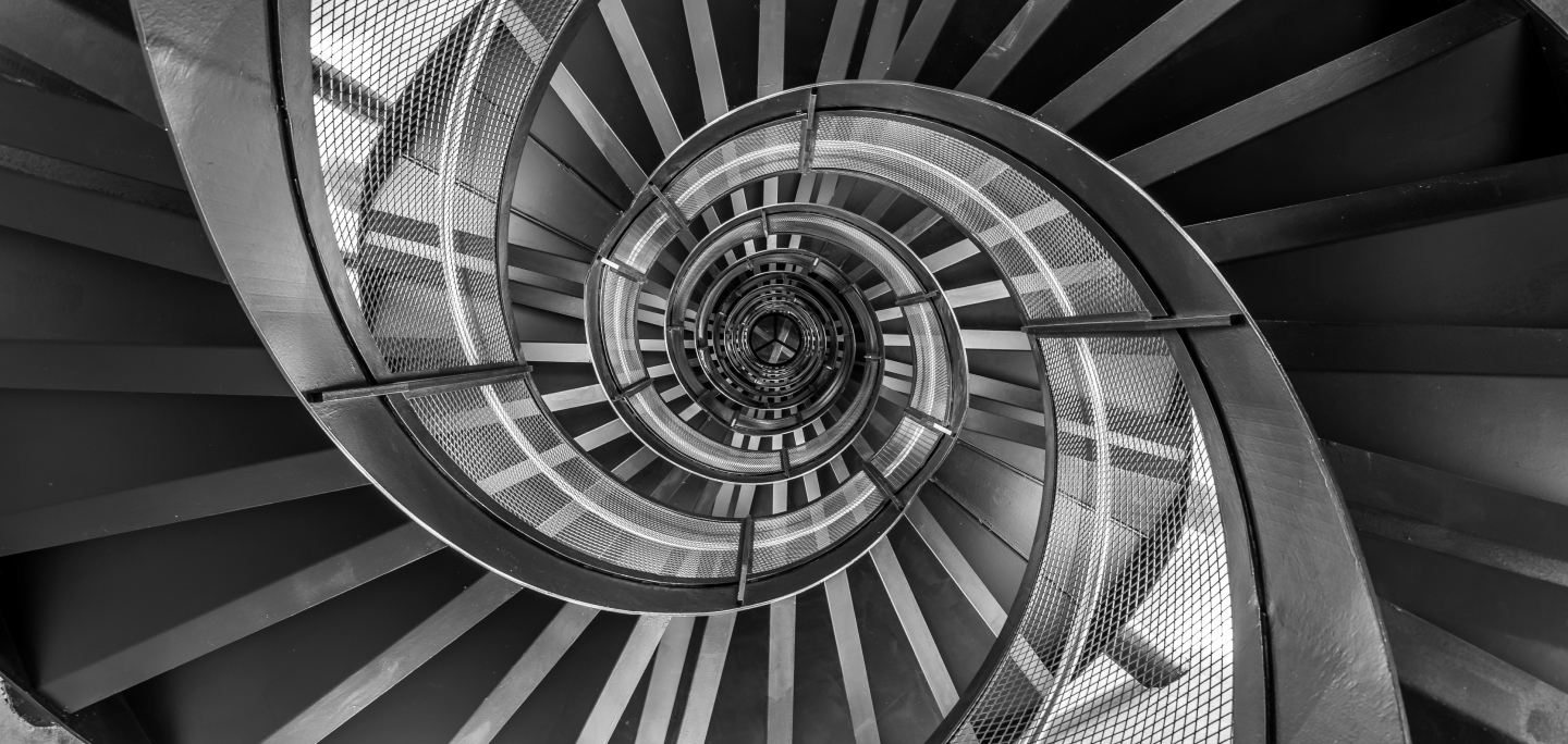 Black and white image of a spiral staircase viewed from above.